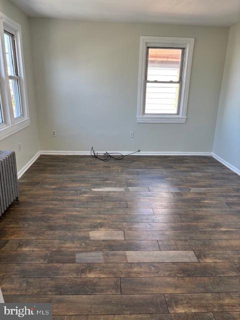 unfurnished room with dark wood finished floors, radiator, and baseboards