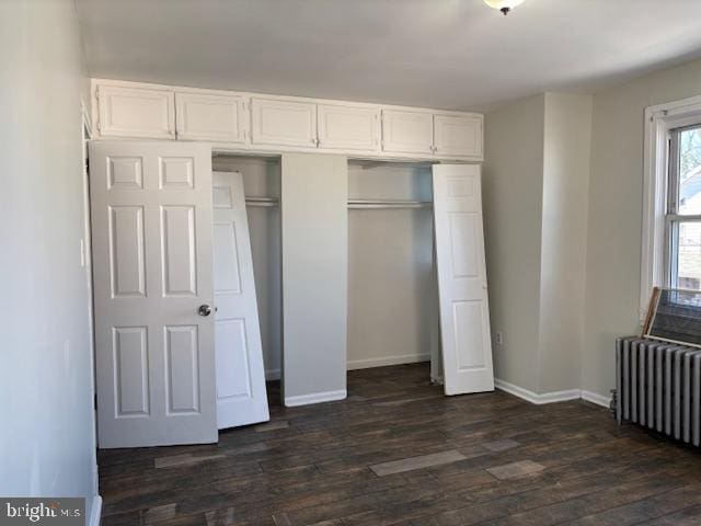 unfurnished bedroom featuring dark wood-style floors, radiator, baseboards, and a closet