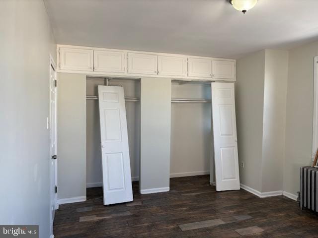 unfurnished bedroom featuring a closet, baseboards, dark wood finished floors, and radiator heating unit