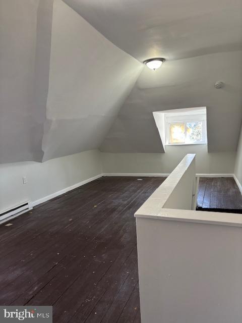 additional living space featuring a baseboard radiator, lofted ceiling, dark wood-type flooring, and baseboards