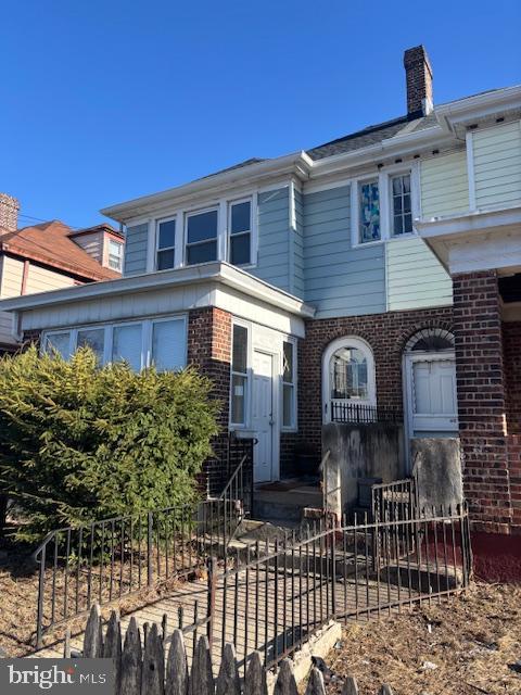 view of front of home with brick siding, a chimney, and fence