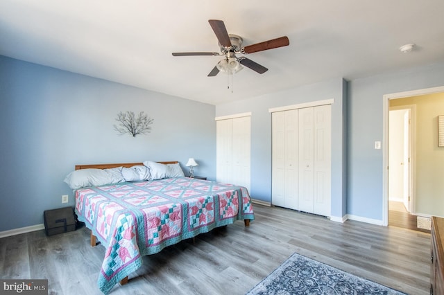 bedroom featuring baseboards, a ceiling fan, multiple closets, and wood finished floors