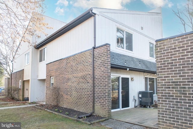 back of house with brick siding, central air condition unit, a shingled roof, and a deck