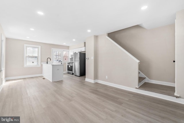 unfurnished living room featuring stairway, light wood-type flooring, baseboards, and a sink