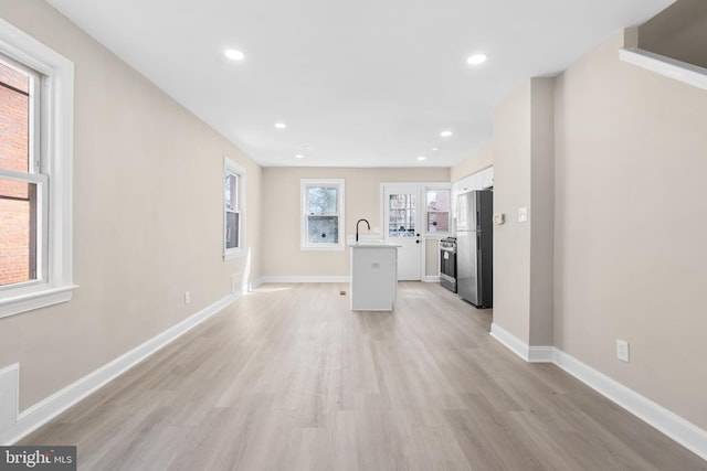 unfurnished living room featuring a sink, baseboards, light wood-style floors, and recessed lighting