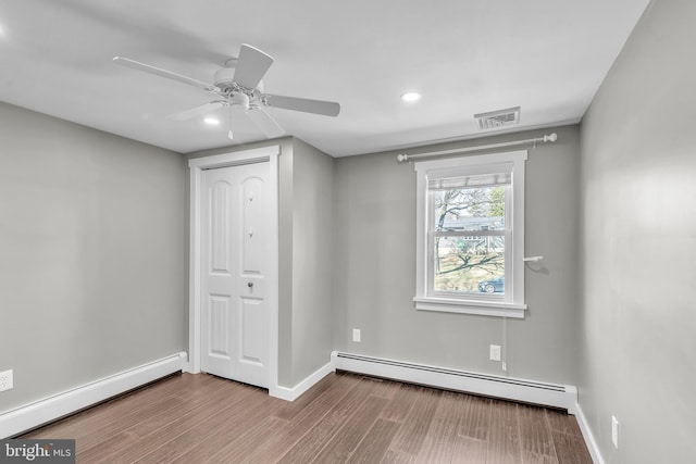 unfurnished bedroom featuring wood finished floors, baseboards, visible vents, and a baseboard radiator