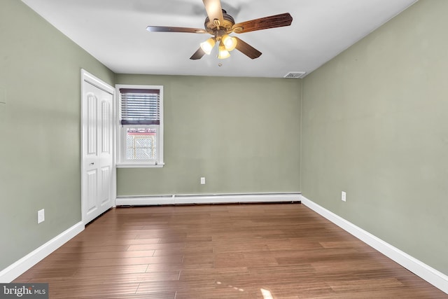 empty room with wood finished floors, baseboards, and a baseboard radiator