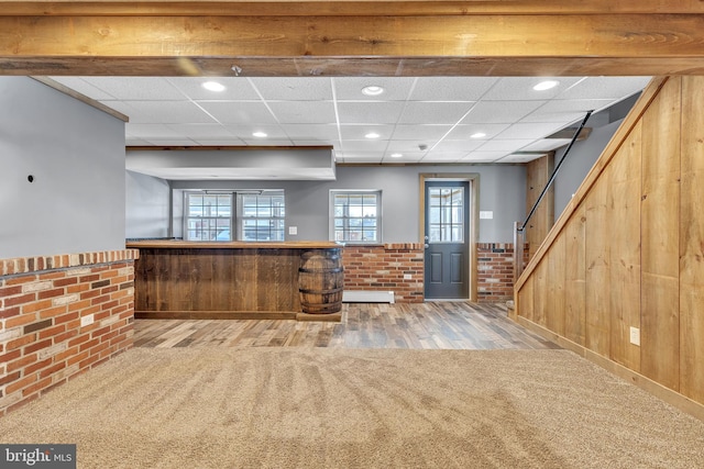 interior space with a drop ceiling, stairway, wood walls, and wainscoting