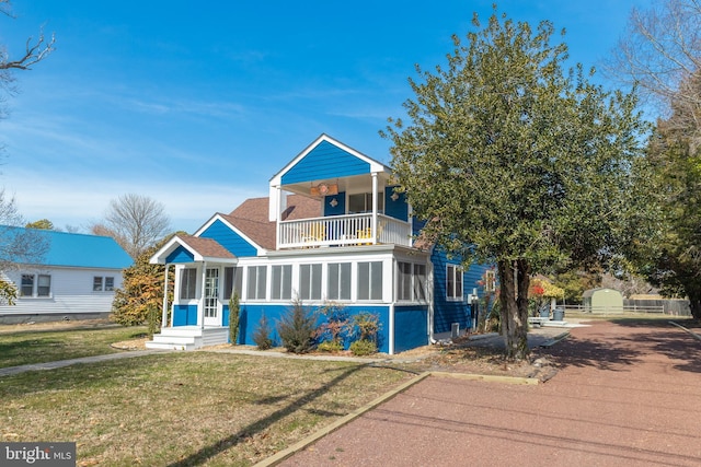 view of front facade featuring a front lawn, a balcony, and a shingled roof