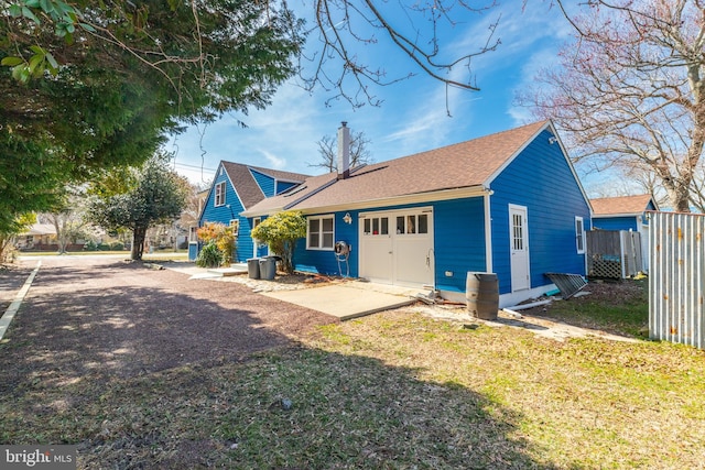 rear view of property featuring a shingled roof, driveway, an attached garage, and fence