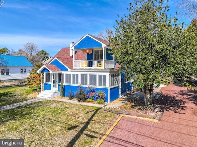 view of front of property featuring a balcony, a chimney, a front lawn, and roof with shingles