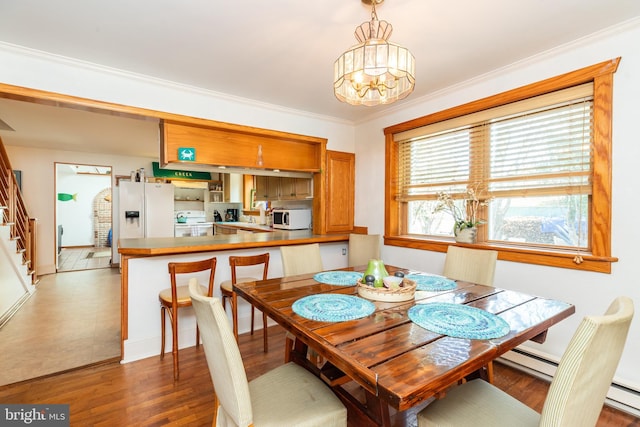 dining area featuring wood finished floors, baseboard heating, ornamental molding, and stairs