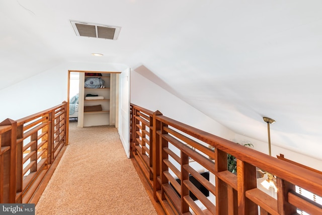 hallway with visible vents, light carpet, an upstairs landing, and vaulted ceiling