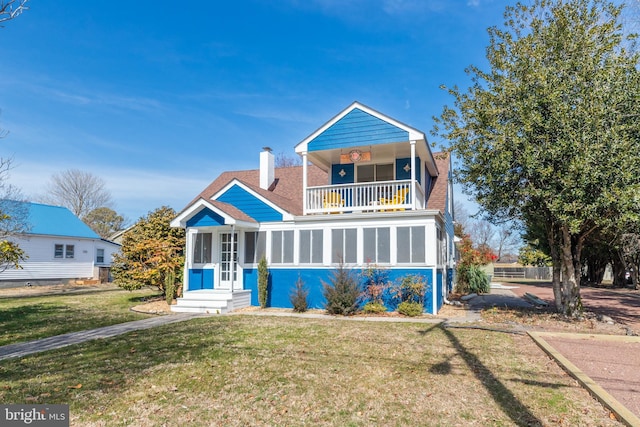 view of front of property with a chimney, a front lawn, a balcony, and a sunroom