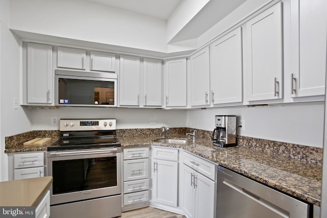 kitchen featuring a sink, dark stone countertops, stainless steel appliances, light wood-style floors, and white cabinets