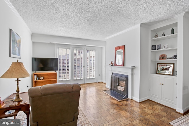 living area featuring built in shelves, a textured ceiling, a glass covered fireplace, crown molding, and baseboards