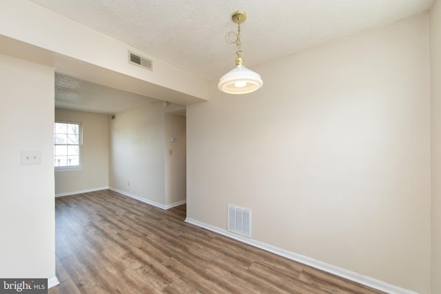 unfurnished room with visible vents, a textured ceiling, and wood finished floors