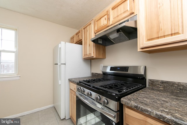 kitchen featuring light brown cabinetry, under cabinet range hood, a textured ceiling, stainless steel range with gas cooktop, and light tile patterned floors