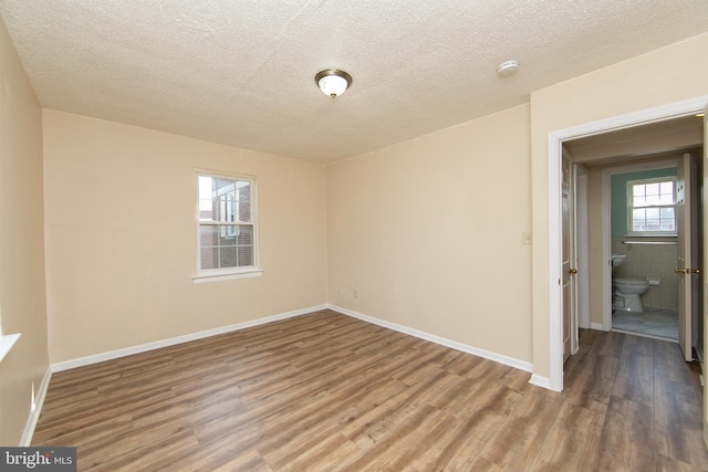 empty room with baseboards, plenty of natural light, a textured ceiling, and wood finished floors