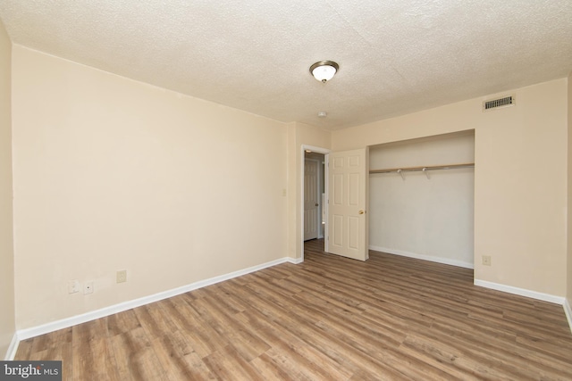 unfurnished bedroom with a closet, visible vents, baseboards, and wood finished floors