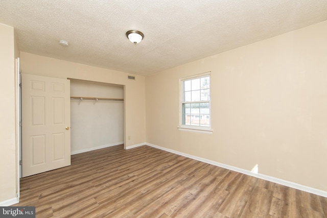 unfurnished bedroom featuring visible vents, a textured ceiling, wood finished floors, a closet, and baseboards