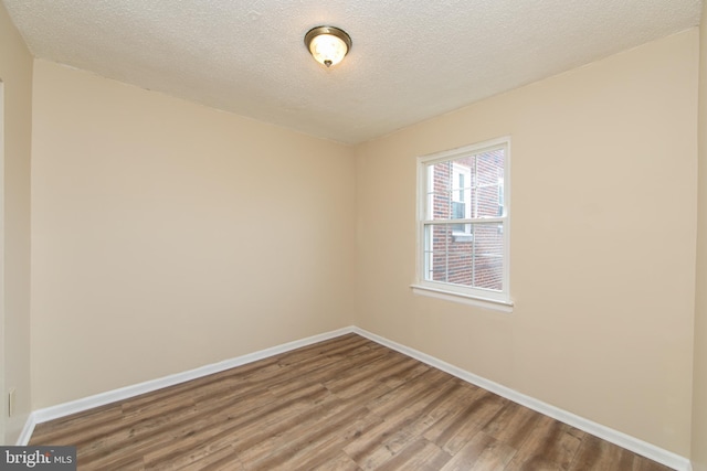 spare room featuring a textured ceiling, baseboards, and wood finished floors