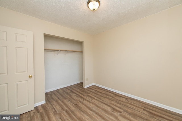 unfurnished bedroom with a closet, baseboards, a textured ceiling, and wood finished floors