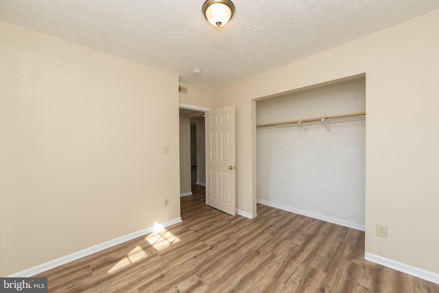 unfurnished bedroom featuring a textured ceiling, wood finished floors, a closet, and baseboards