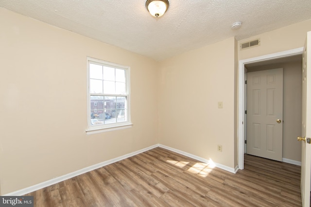 unfurnished room featuring visible vents, a textured ceiling, baseboards, and wood finished floors