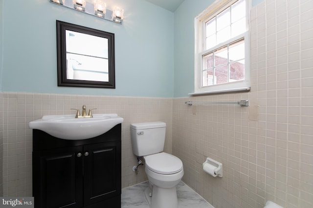 bathroom featuring a wainscoted wall, toilet, marble finish floor, tile walls, and vanity