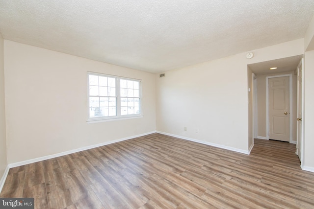 unfurnished room featuring visible vents, a textured ceiling, light wood-type flooring, and baseboards