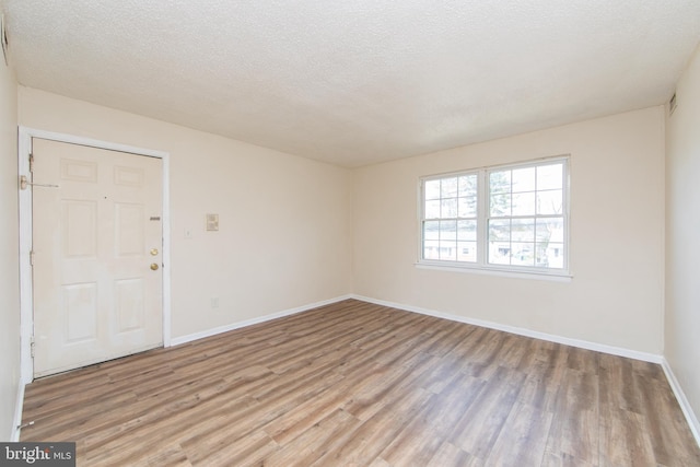 empty room featuring baseboards, a textured ceiling, and light wood-style floors