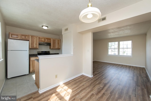 kitchen with baseboards, visible vents, freestanding refrigerator, under cabinet range hood, and light wood-type flooring