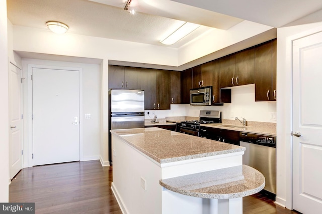 kitchen with dark wood-style floors, a sink, dark brown cabinetry, appliances with stainless steel finishes, and a center island