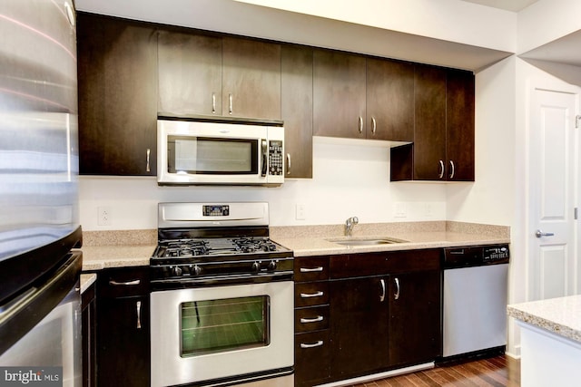 kitchen featuring dark wood-type flooring, light stone countertops, dark brown cabinetry, appliances with stainless steel finishes, and a sink