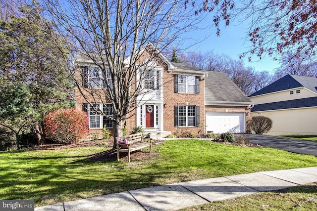 colonial-style house with aphalt driveway, an attached garage, a front lawn, and brick siding