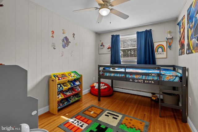 bedroom featuring a ceiling fan, wood finished floors, baseboards, and a baseboard radiator