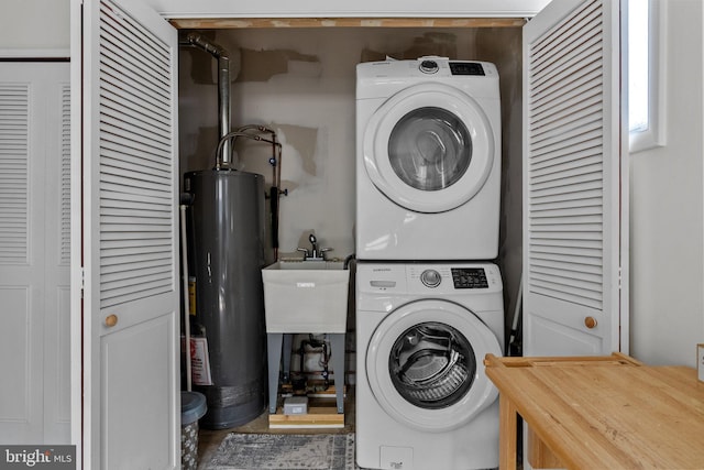 clothes washing area featuring a sink, gas water heater, stacked washer / dryer, and laundry area