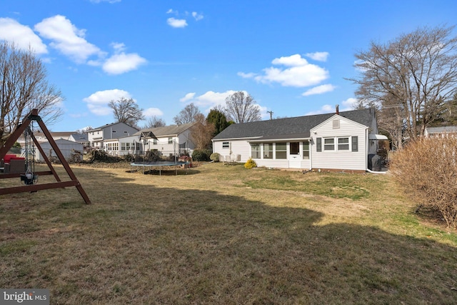 back of house with a lawn, a playground, a trampoline, and a sunroom