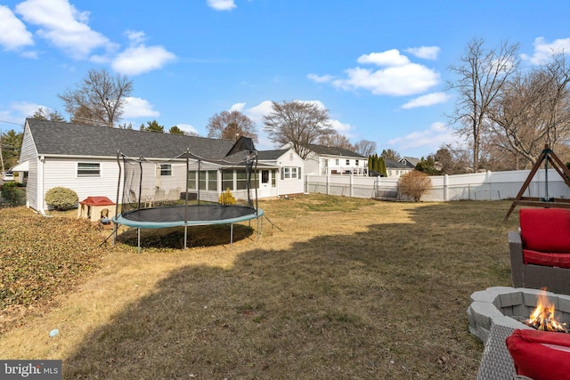 back of property with a trampoline, an outdoor fire pit, a lawn, a fenced backyard, and a sunroom