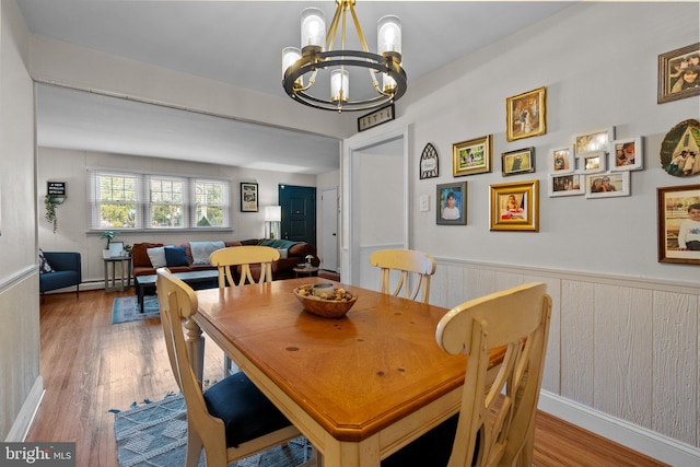 dining area featuring an inviting chandelier, wood finished floors, and wainscoting