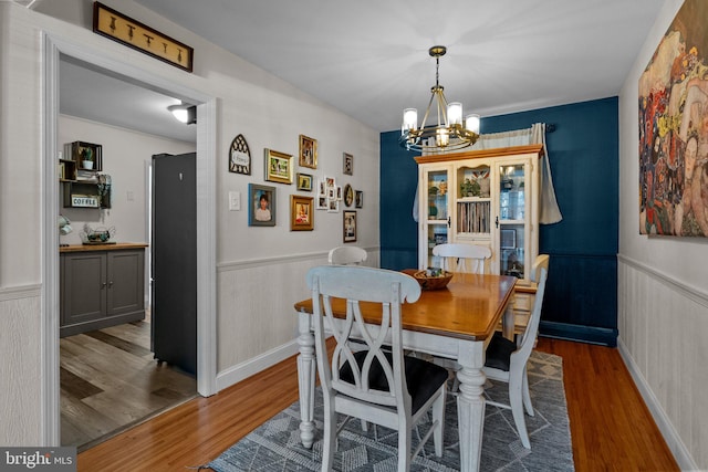 dining space featuring a wainscoted wall, a notable chandelier, and wood finished floors