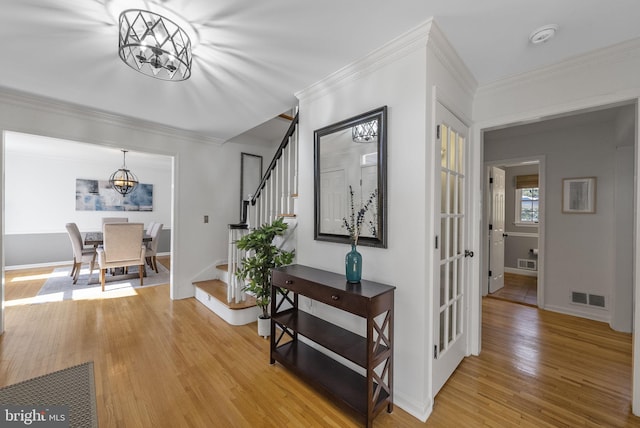 hallway featuring visible vents, crown molding, stairway, light wood-type flooring, and an inviting chandelier