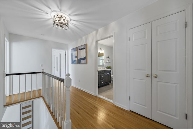 hallway with a sink, baseboards, an upstairs landing, and light wood-style flooring