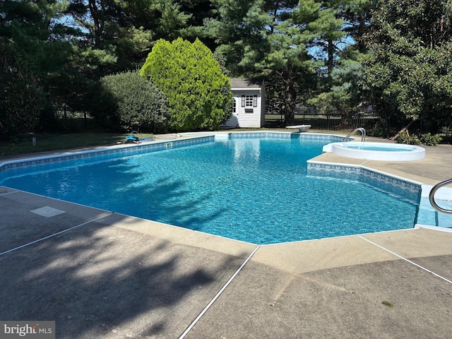 pool featuring fence, a patio area, an outbuilding, an in ground hot tub, and a diving board