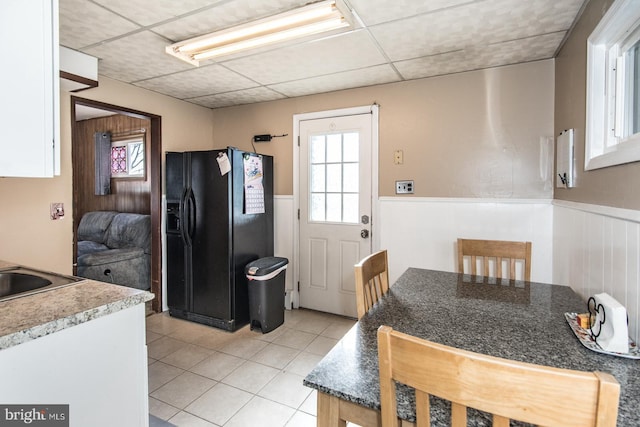 kitchen featuring light tile patterned floors, wainscoting, a paneled ceiling, and black refrigerator with ice dispenser