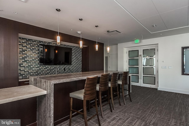 bar featuring baseboards, pendant lighting, dark carpet, and a community bar