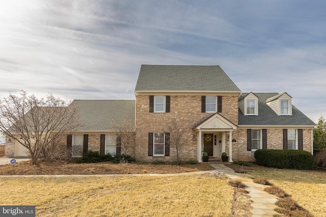 view of front facade with a front yard, brick siding, and a shingled roof