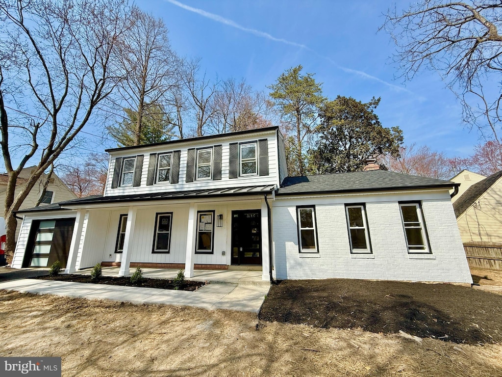 view of front facade featuring a chimney, brick siding, covered porch, and an attached garage