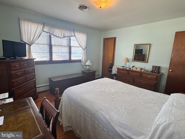 bedroom featuring visible vents, a baseboard heating unit, and wood finished floors